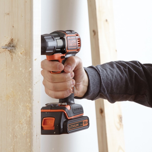Perceuse sans fil BLACK+DECKER ASD184K en usage, perçant du bois, vue latérale, batterie lithium 18V visible.