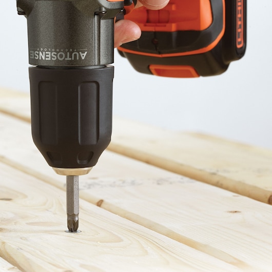 Photo de la perceuse sans fil BLACKDECKER ASD184K vissant une vis dans une surface en bois clair, vue en gros plan.