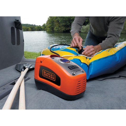 BLACKDECKER ASI300 draagbare oranje luchtcompressor blaast een blauw-geel vlot op bij een meer.