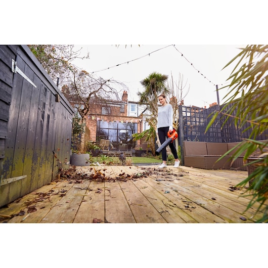 Foto van de BLACKDECKER BCBL200B bladblazer in gebruik op een houten terras in een tuin.