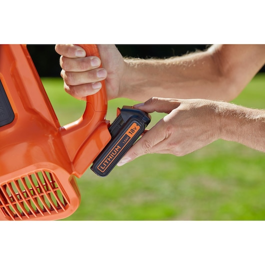 Close-up foto van BLACKDECKER BCBL200B bladblazer met hand die 18V lithium accu buiten plaatst.