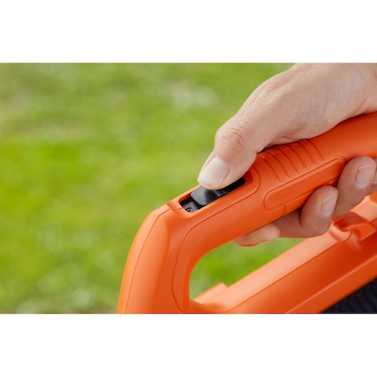 Close-up foto van een hand die op de aan/uit-knop van het oranje BLACKDECKER BCBL200B blazerhandvat drukt.