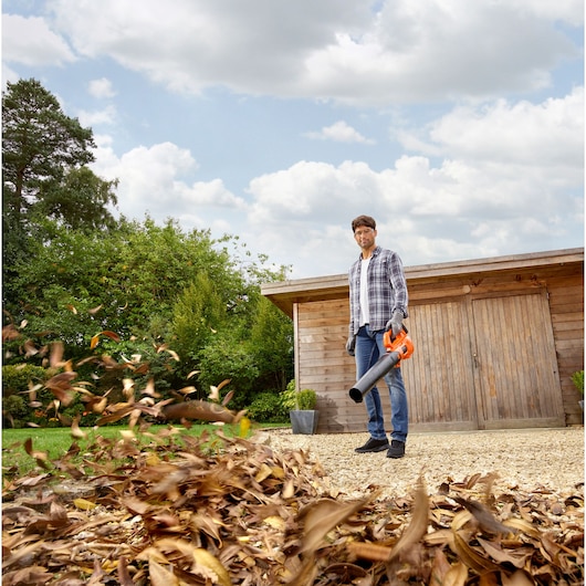 BLACKDECKER BCBL200L bladblazer in gebruik, persoon verwijdert droge bladeren van grindpad.