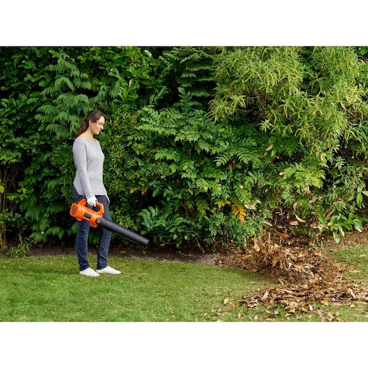 BLACKDECKER BCBL200L bladblazer in gebruik buiten, oranje en zwart ontwerp, blaast bladeren op gras.