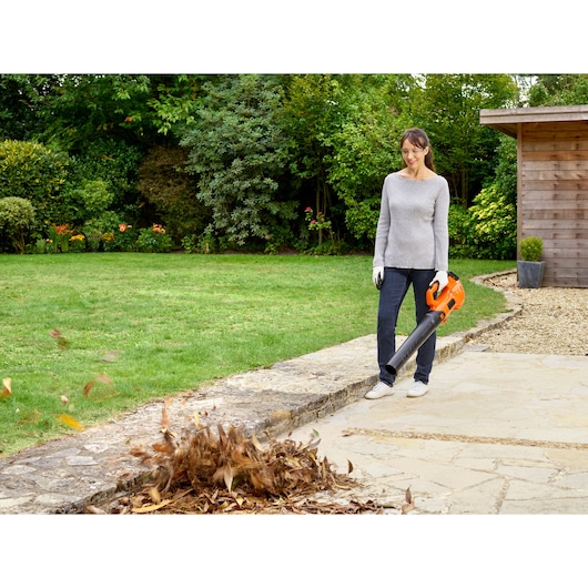 BLACKDECKER BCBL200L draadloze bladblazer buiten in gebruik, oranje, blaast bladeren op stenen pad.