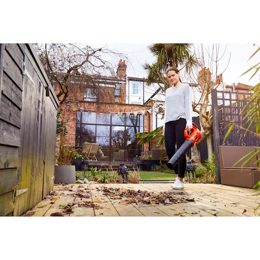BLACKDECKER BCBL200L bladblazer vastgehouden door persoon die bladeren verwijdert op houten terras in de tuin.