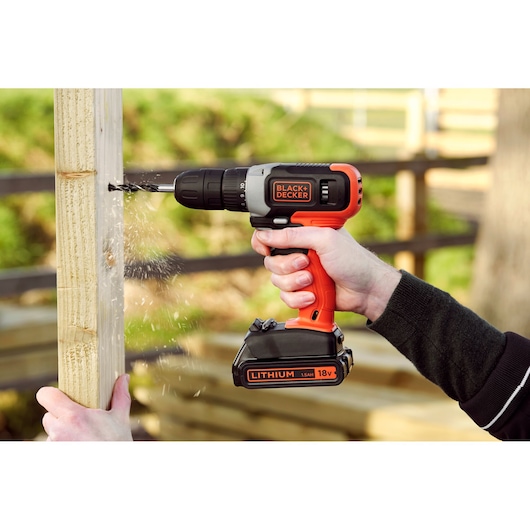 Photo de la perceuse sans fil 18V BLACK+DECKER BCD001C2 en utilisation pour percer du bois en extérieur.