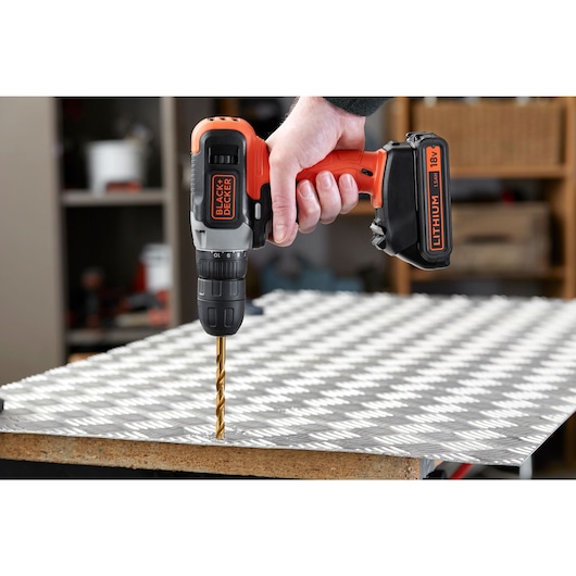 BLACKDECKER perceuse sans fil BCD001C2 perçant une plaque métallique, angle latéral, orange et noir.