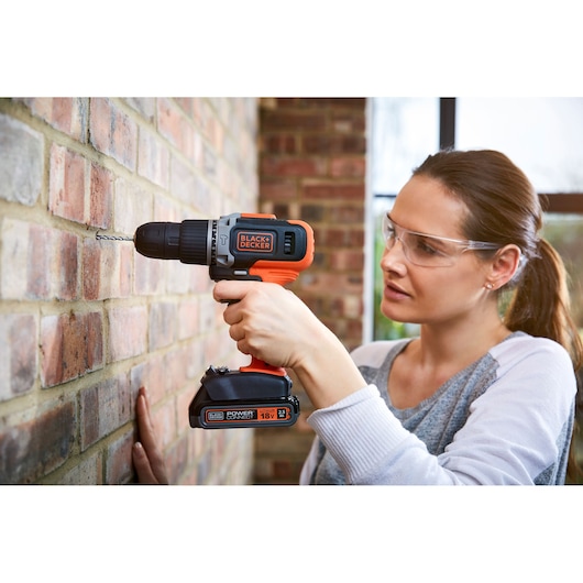 Photo de la perceuse sans fil BLACK+DECKER BCD003C1 en utilisation perçant un mur en briques, vue rapprochée.