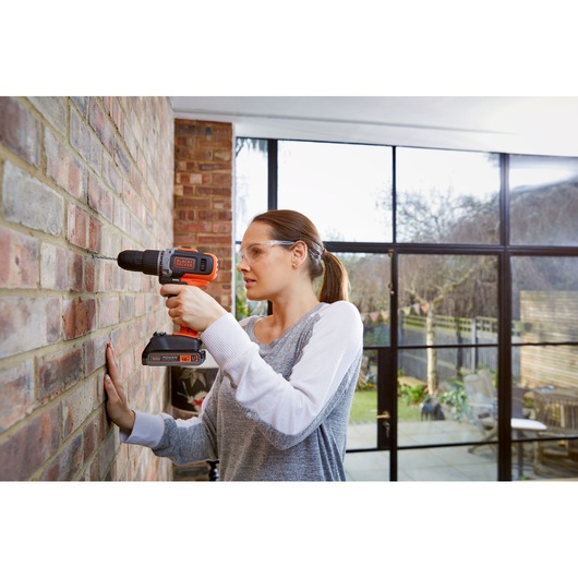 Perceuse sans fil BLACKDECKER BCD003C1 utilisée sur mur en brique, produit en main, batterie visible