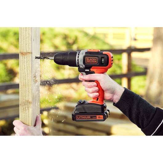 Perceuse sans fil BLACK+DECKER BCD003C2K en utilisation, perçant un poteau en bois à l’extérieur.