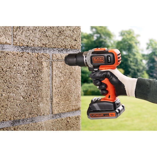 BLACKDECKER BCD003ME2K perceuse sans fil utilisée sur mur en béton à l'extérieur, corps orange et noir.