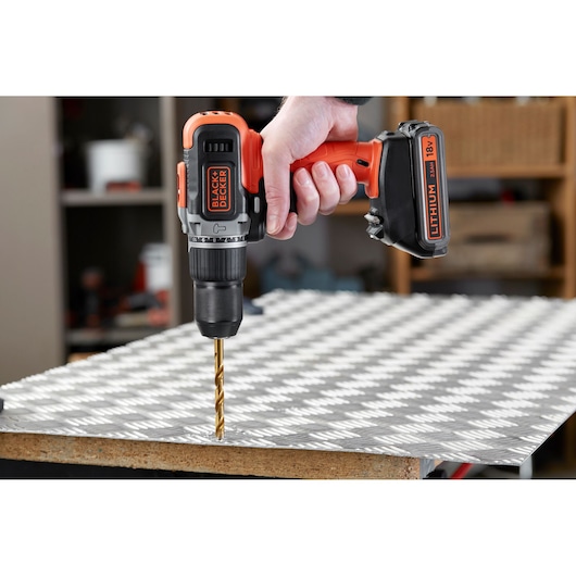 Perceuse sans fil BLACK+DECKER BCD003MEM2K orange et noire utilisée pour percer une plaque métallique, vue latérale rapprochée.