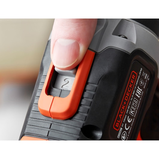 Gros plan sur le sélecteur de vitesse de perceuse BLACK+DECKER BCD003MEM2K avec un doigt, noir et orange.