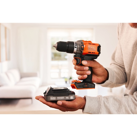 BLACKDECKER BCD383D1 perceuse sans fil et batterie tenues en main, présentées dans un salon lumineux.