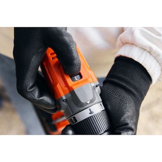 Photo en gros plan de la perceuse BLACKDECKER BCD383D1, main ajustant les réglages, corps orange et gris.