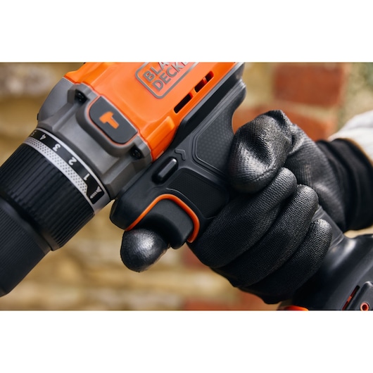 Photo de la perceuse sans fil BLACKDECKER BCD383D1 tenue par une main gantée, focus sur la gâchette et la poignée.