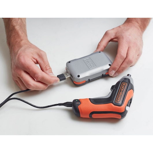 Photographie du tournevis sans fil BLACK+DECKER BCF611CK en charge via un câble USB connecté à une batterie externe argentée.