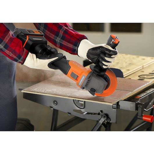 BLACKDECKER BCG6L8F1S meuleuse d’angle sans fil découpant un carreau sur un établi, utilisateur avec gants.