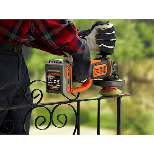 BLACKDECKER BCG720M1 draadloze haakse slijper op metalen hek buiten, oranje en zwart ontwerp.