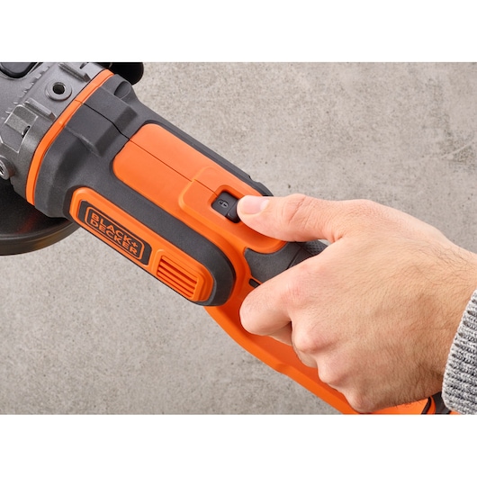Close-up van een hand die de aan/uit-schakelaar bedient op een BLACK+DECKER BCG720N accu-haakse slijper.