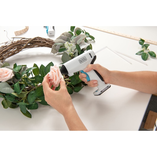 Foto van BLACKDECKER BCGL115 draadloze lijmpistool gebruikt om een bloem aan een krans te bevestigen.
