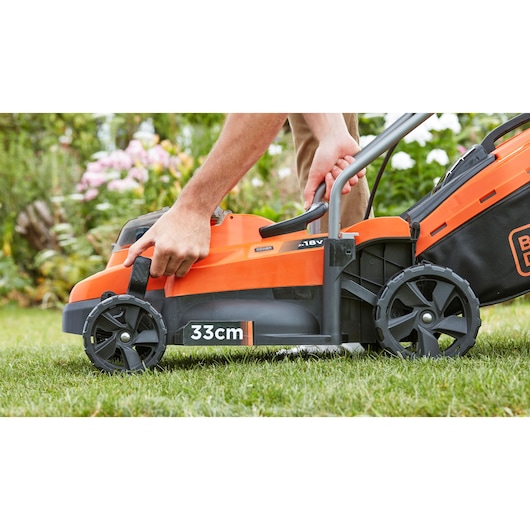 Tondeuse BLACKDECKER BCMW33185L2 vue de côté, orange et noire, largeur de coupe 33cm, utilisateur ajustant la poignée dehors.