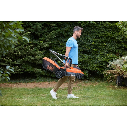 Photo de la tondeuse BLACKDECKER BCMW3318N orange et noire portée à l'extérieur par une personne.