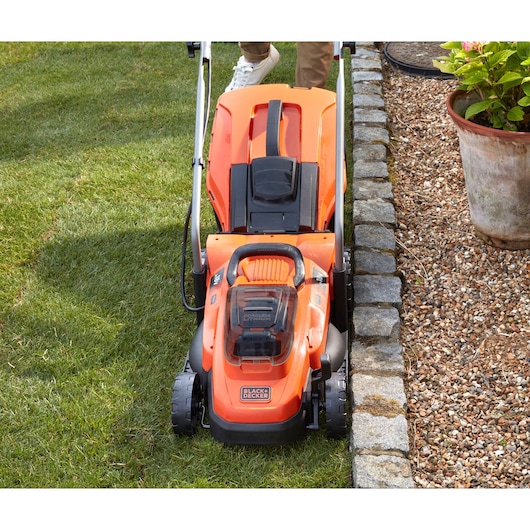 BLACKDECKER BCMW3318N tondeuse à gazon sans fil vue de dessus sur l’herbe près d’une bordure en pierre.