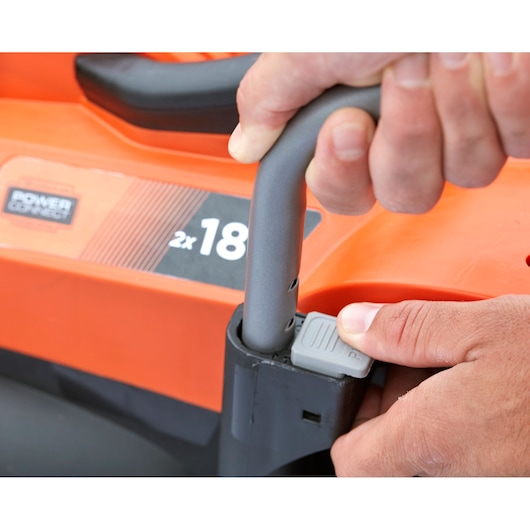 Gros plan sur le réglage de la poignée de la tondeuse BLACKDECKER BCMW3318N avec mains, corps orange et noir visible.