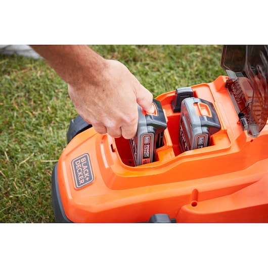 Photo d'une tondeuse BLACKDECKER BCMW3318N avec une main insérant une batterie 18V dans le compartiment orange.