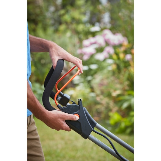 Gros plan sur la poignée de tondeuse BLACKDECKER BCMW3318N avec les mains de l'utilisateur dans un jardin.