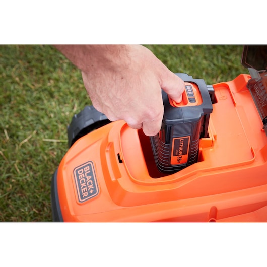 Photo de la batterie de tondeuse BLACK+DECKER BCMW3336L1 insérée dans le corps orange de la tondeuse.