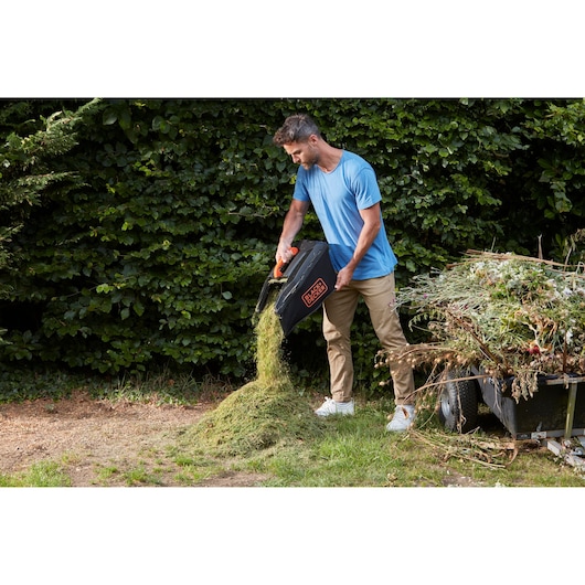 Bac de récupération d’herbe de la tondeuse BLACKDECKER BCMW3336N vidé par une personne en extérieur.