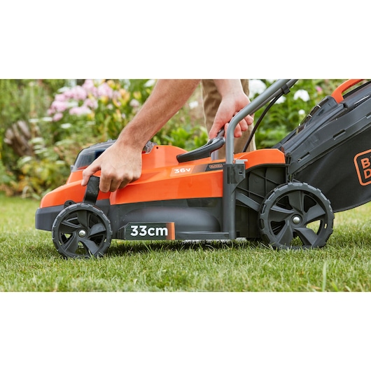 Photo de la tondeuse sans fil BLACKDECKER BCMW3336N, largeur de coupe 33cm, gros plan sur le réglage du manche au jardin.