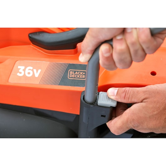 Gros plan sur des mains ajustant la poignée de la tondeuse 36V BLACK+DECKER BCMW3336N avec corps orange.