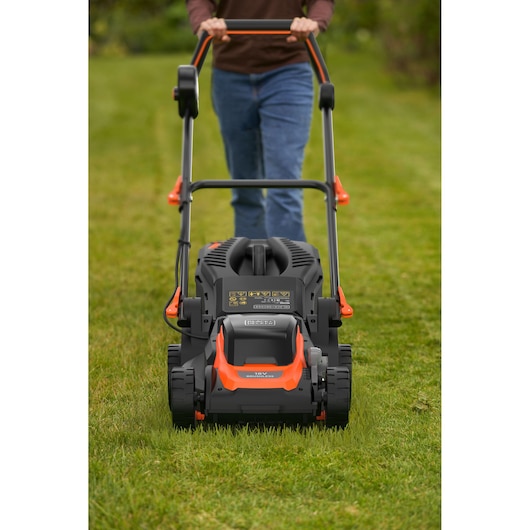 Een persoon duwt een BLACK+DECKER grasmaaier over een groen gazon. De afbeelding toont de voorkant van de maaier met de persoon erachter die de handgrepen vasthoudt.