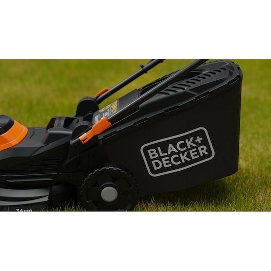 Close-up van een BLACK+DECKER grasmaaier op gras, waarbij de zijkant en het achterwiel met het duidelijk zichtbare merklogo te zien zijn.