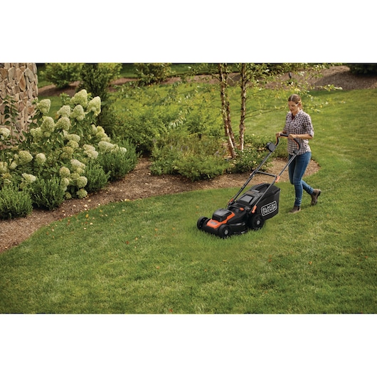 Een persoon maait het gras met een BLACK+DECKER elektrische grasmaaier in een groene tuin.