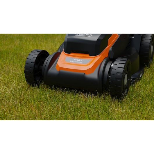 Close-up van een draadloze grasmaaier van BLACK+DECKER met een oranje en zwarte behuizing op groen gras. Het label op de maaier luidt '2x18V Brushless'.