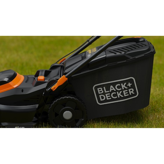 Close-up van een BLACK+DECKER grasmaaier op groen gras, met het merklogo en een deel van het wiel zichtbaar.