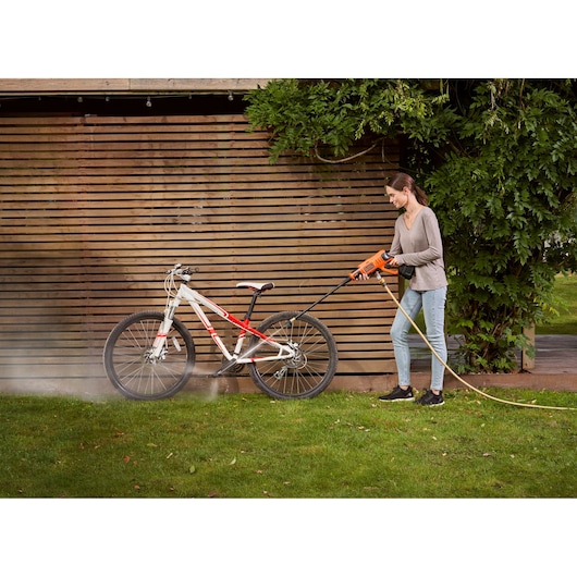 BLACKDECKER BCPC18B hogedrukreiniger reinigt een fiets buiten op gras naast een houten schutting.
