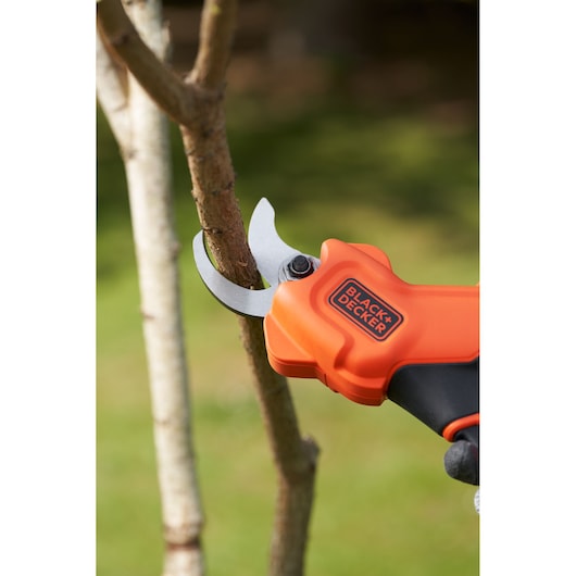 BLACK+DECKER BCPP18D1 oranje snoeischaar op accu knipt een tak buiten.