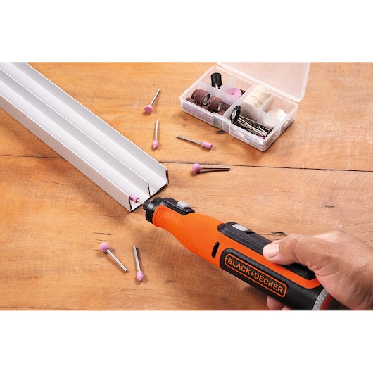 BLACK+DECKER BCRT8IK roterende gereedschapsset met oranje handgreep in gebruik op metaal, diverse accessoires en doos op tafel.
