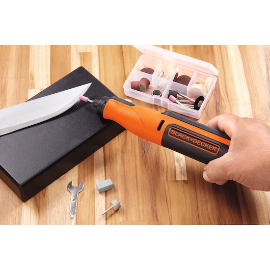 BLACK+DECKER BCRT8IK roterend gereedschap in gebruik om mes te slijpen, met accessoirekit en hulpstukken op houten tafel, zijaanzicht.