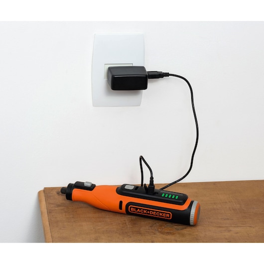 Oranje BLACK+DECKER BCRT8IK draadloos roterend gereedschap aan het opladen op een houten tafel.