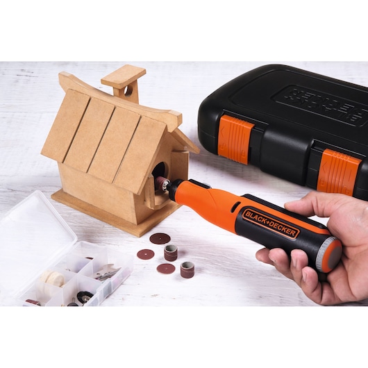 BLACK+DECKER BCRT8IK rotatiegereedschap gebruikt op houten vogelhuisje met accessoiredoos en zwart-oranje opbergbox.