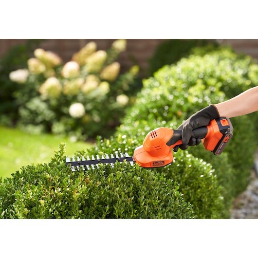 BLACKDECKER BCSS18B cisaille à arbustes sans fil orange et noire, taille de buissons verts en extérieur.