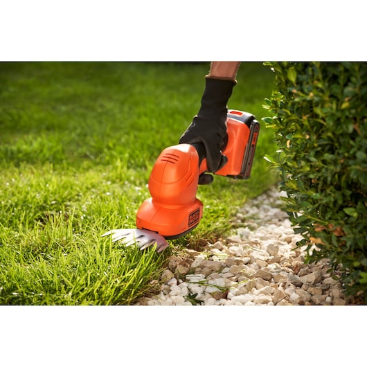 BLACKDECKER BCSS18B cisaille à gazon sans fil taillant le bord de la pelouse près des buissons et des pierres.