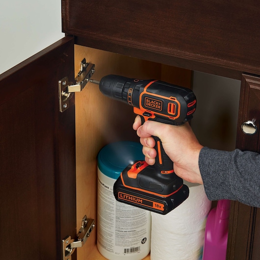 BLACKDECKER BDC718AS2O perceuse sans fil noire et orange utilisée pour fixer une charnière d’armoire.